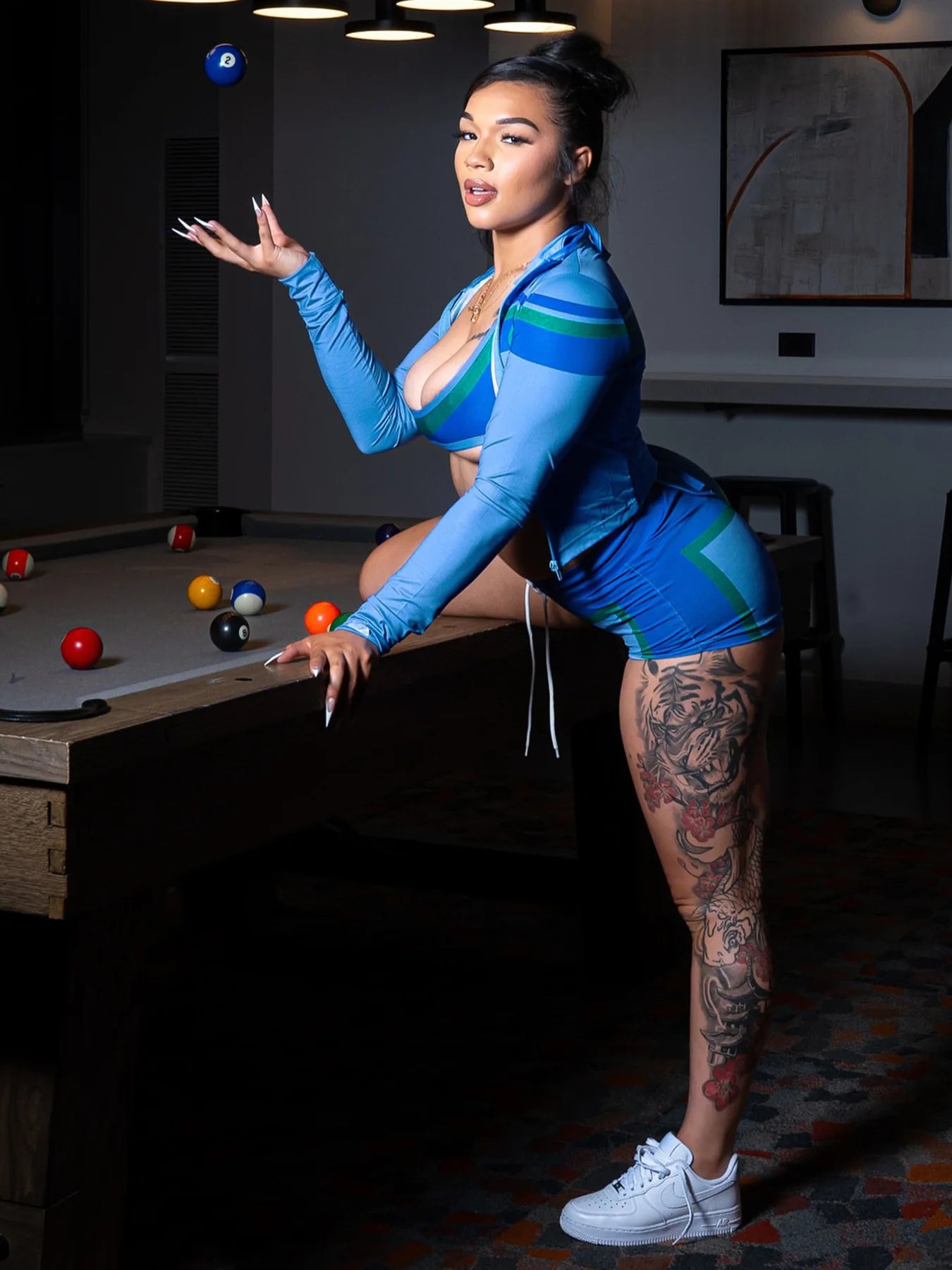 Woman in a blue and green outfit standing next to a pool table with pool balls.